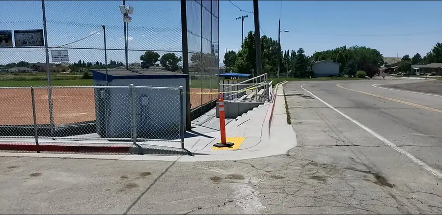 New concrete sidewalk and ramp with a yellow detectable warning pad where the ballfield meets the street