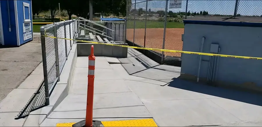 New concrete ramp leading to the bleachers behind a ballfield's chain-link backstop