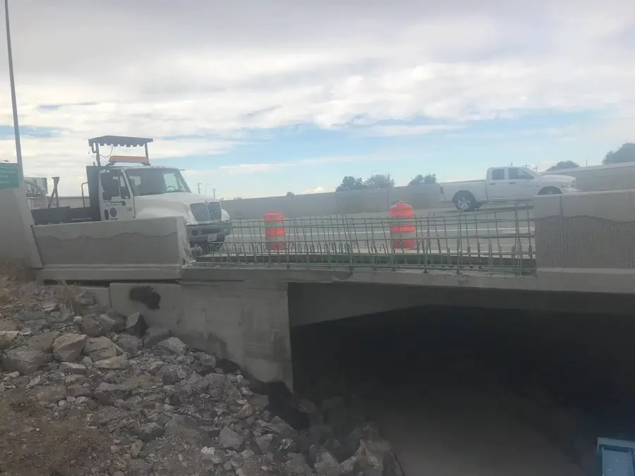 Bridge railing removed down to exposed rebar, with traffic barrels and work trucks on the deck