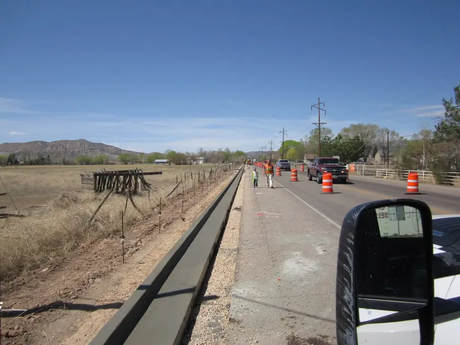 Long run of new concrete curb and gutter beside a rural road, with crew members walking the coned-off lane