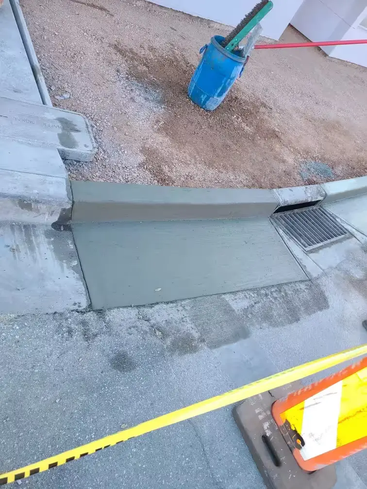 New section of curb and gutter poured up to a storm drain inlet, with caution tape and a barricade in front