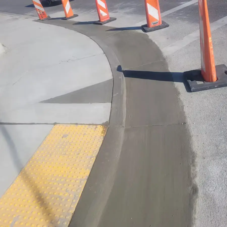 New concrete curb and gutter wrapping a corner beside a sidewalk ramp with a yellow detectable warning pad