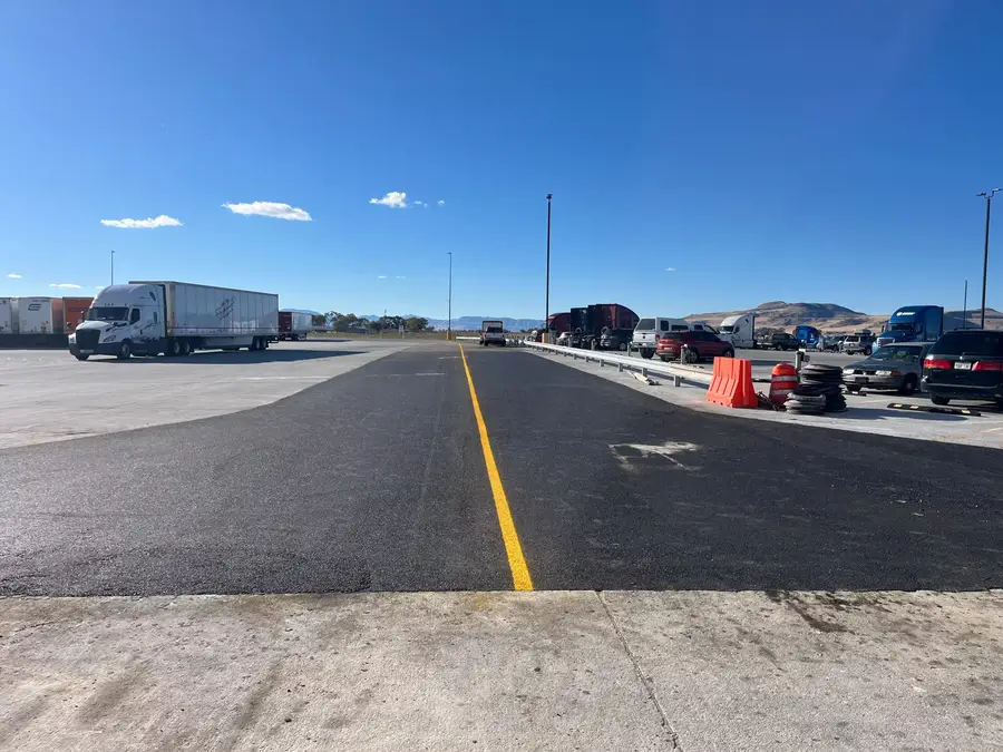 A freshly paved asphalt lane with a new yellow center line through a truck parking lot