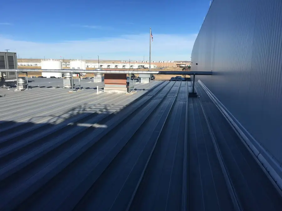 Standing seam metal roof running along the wall of a large commercial building, with rooftop pipes and vents