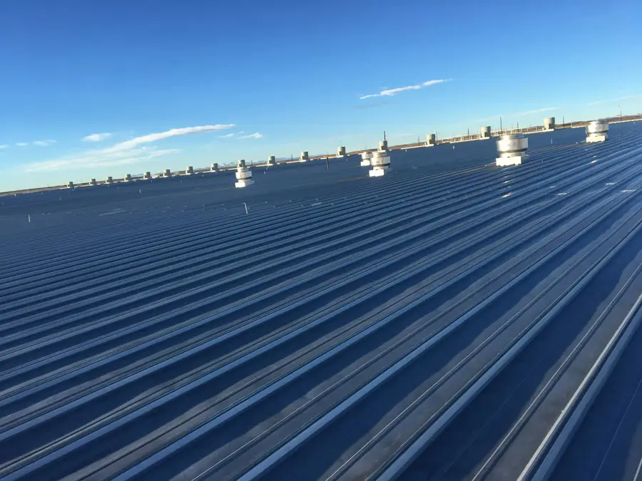 Wide standing seam metal roof with rows of round roof vents under a clear blue sky
