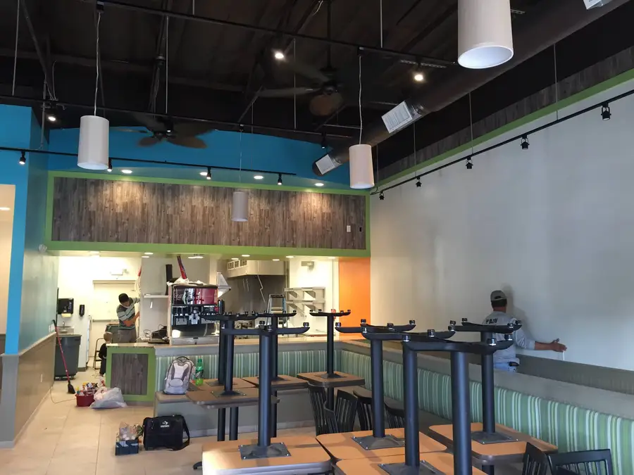 Finished Rumbi Island Grill dining room with blue and green walls, pendant lights, striped booth seating and the order counter