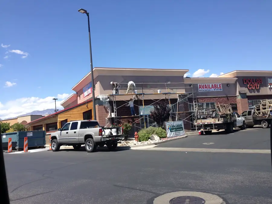 Workers on scaffolding at the storefront of the Rumbi Island Grill space during exterior work