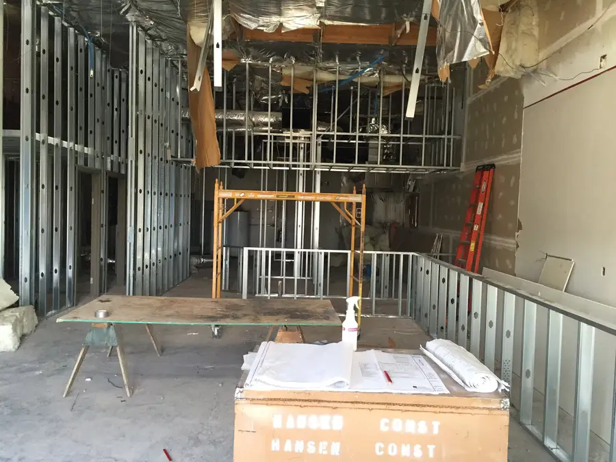 New metal stud framing inside the restaurant, with plans laid out on a B Hansen Construction job box