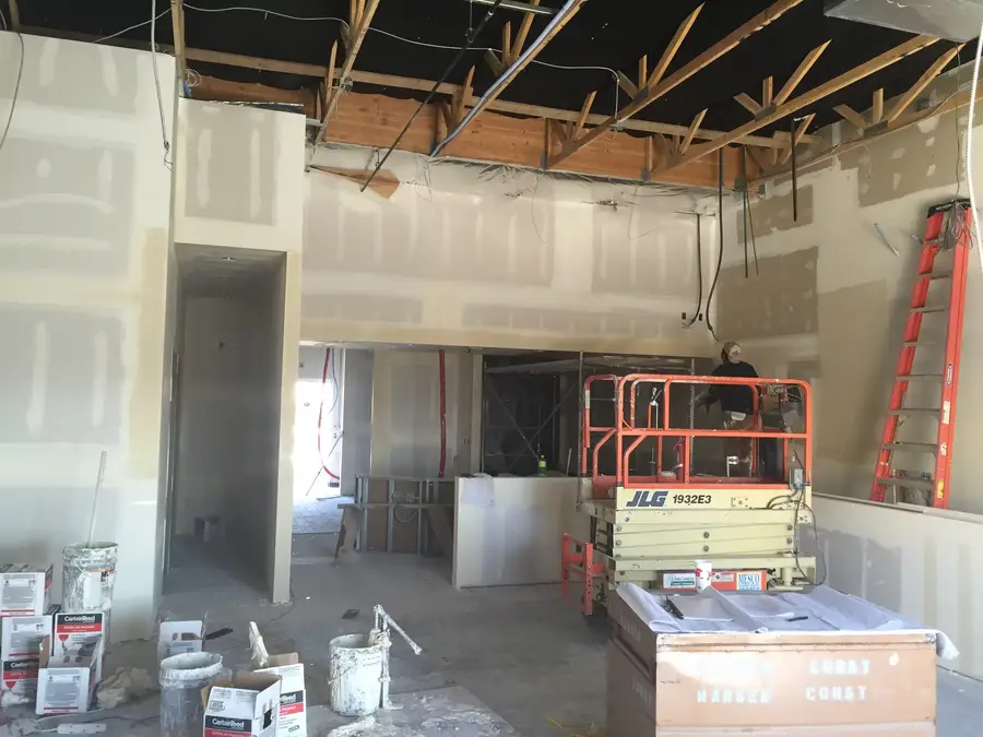 Drywall going up inside the restaurant, with a scissor lift, ladder and buckets of joint compound