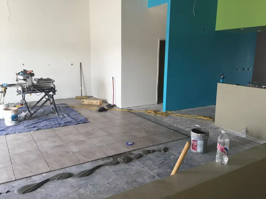 Floor tile partly laid beside a blue accent wall, with the tile saw on a drop cloth
