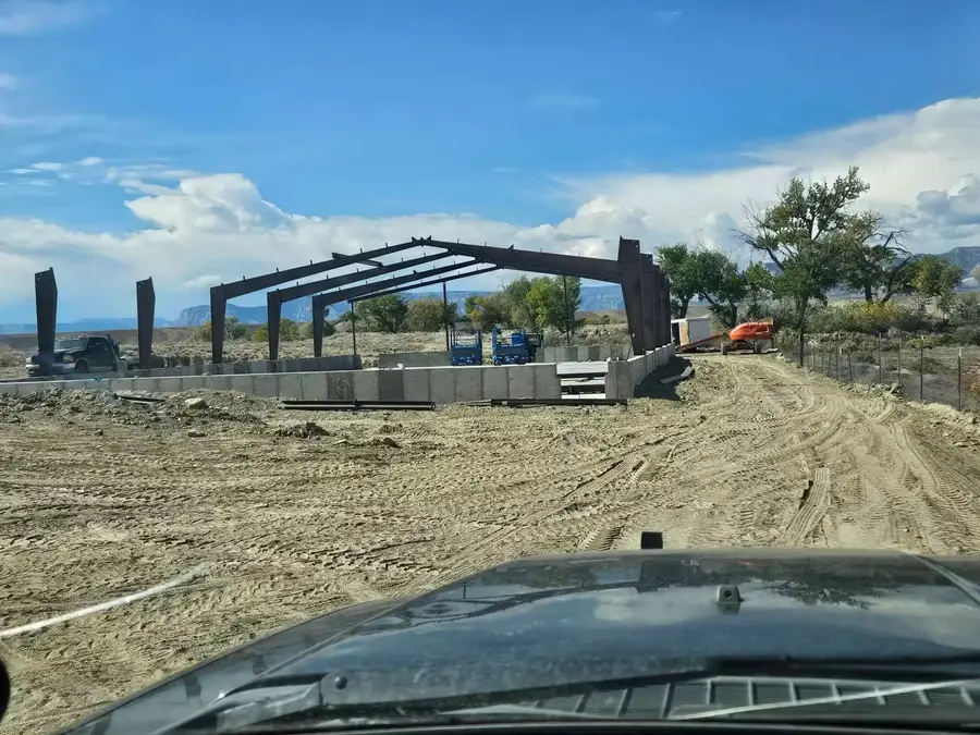 Steel columns and rafters rising on a new concrete foundation, seen from a truck on the dirt access road