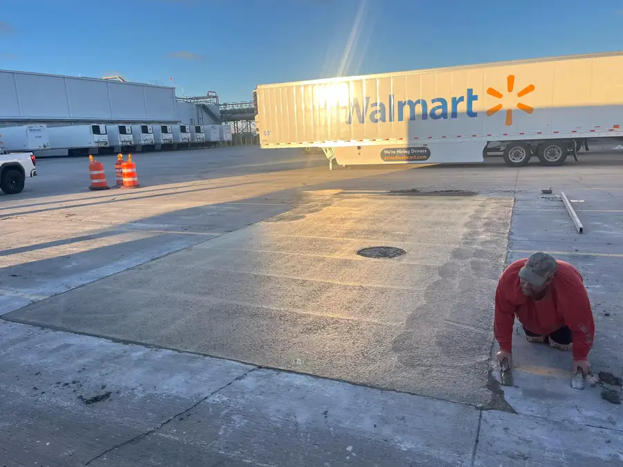Worker hand-finishing a concrete repair in the morning light next to a Walmart trailer