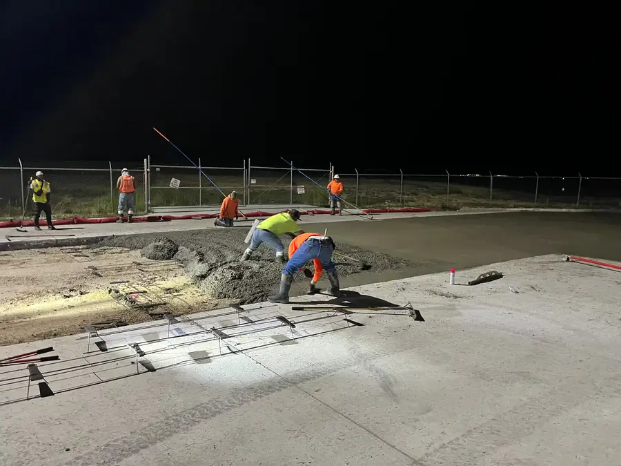Crew screeding and finishing a fresh concrete pour under work lights at night