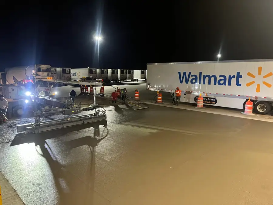 Night paving work beside a Walmart trailer with the dock lights on