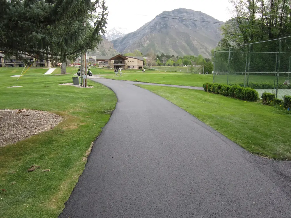 A freshly paved asphalt path curving across a lawn toward the mountains