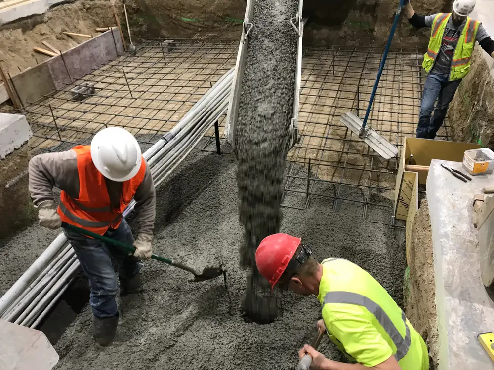 Crew placing concrete in a trench over rebar and a bank of white pipes