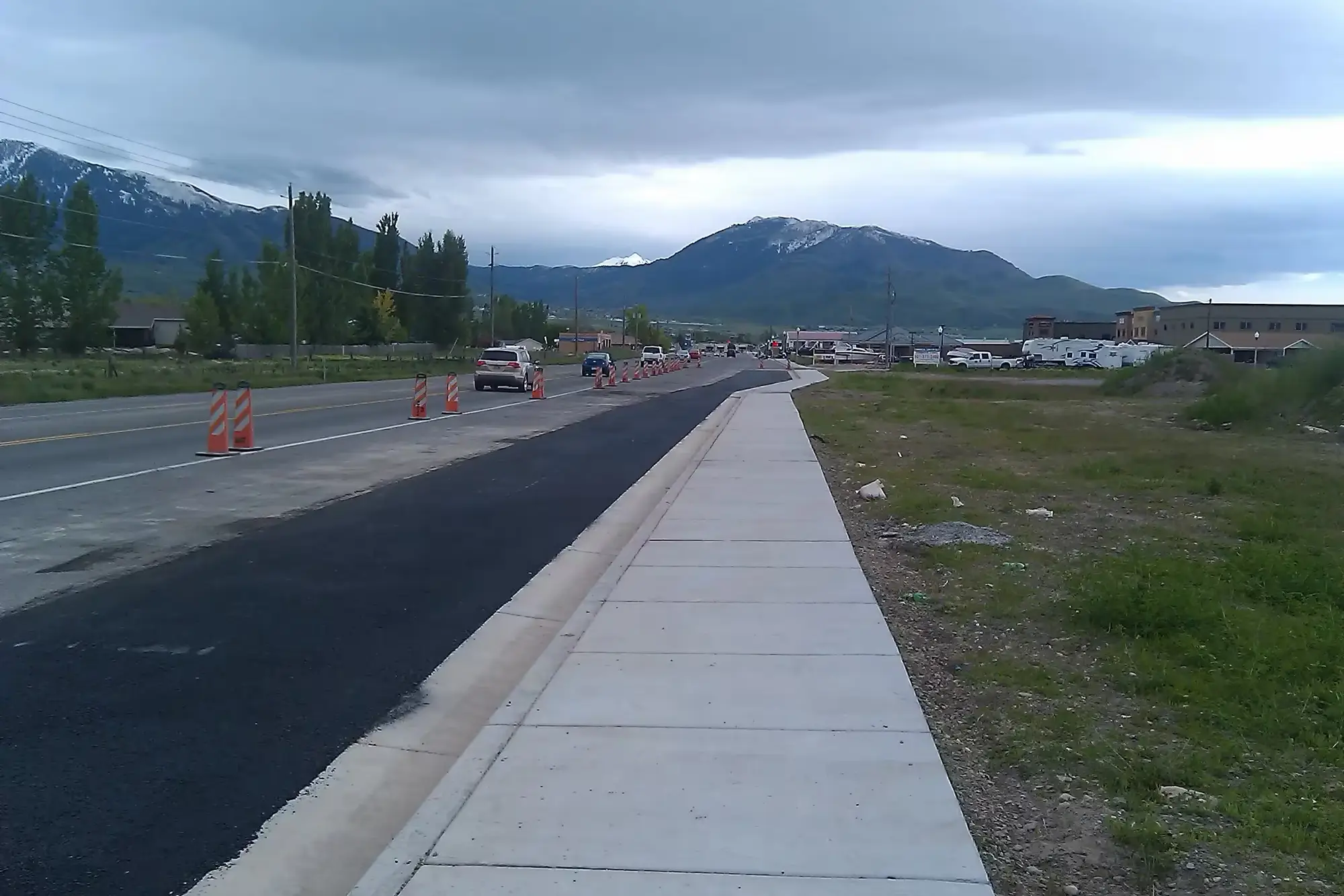 New concrete sidewalk beside a freshly paved road, with mountains behind