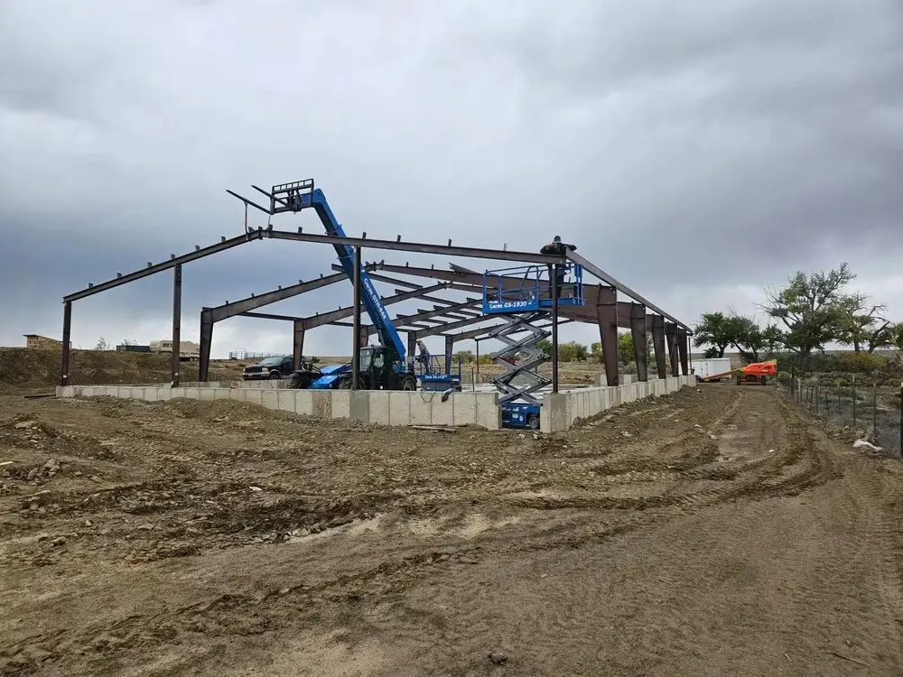 Steel frame of a commercial building going up on a concrete stem wall, with a telehandler and scissor lift