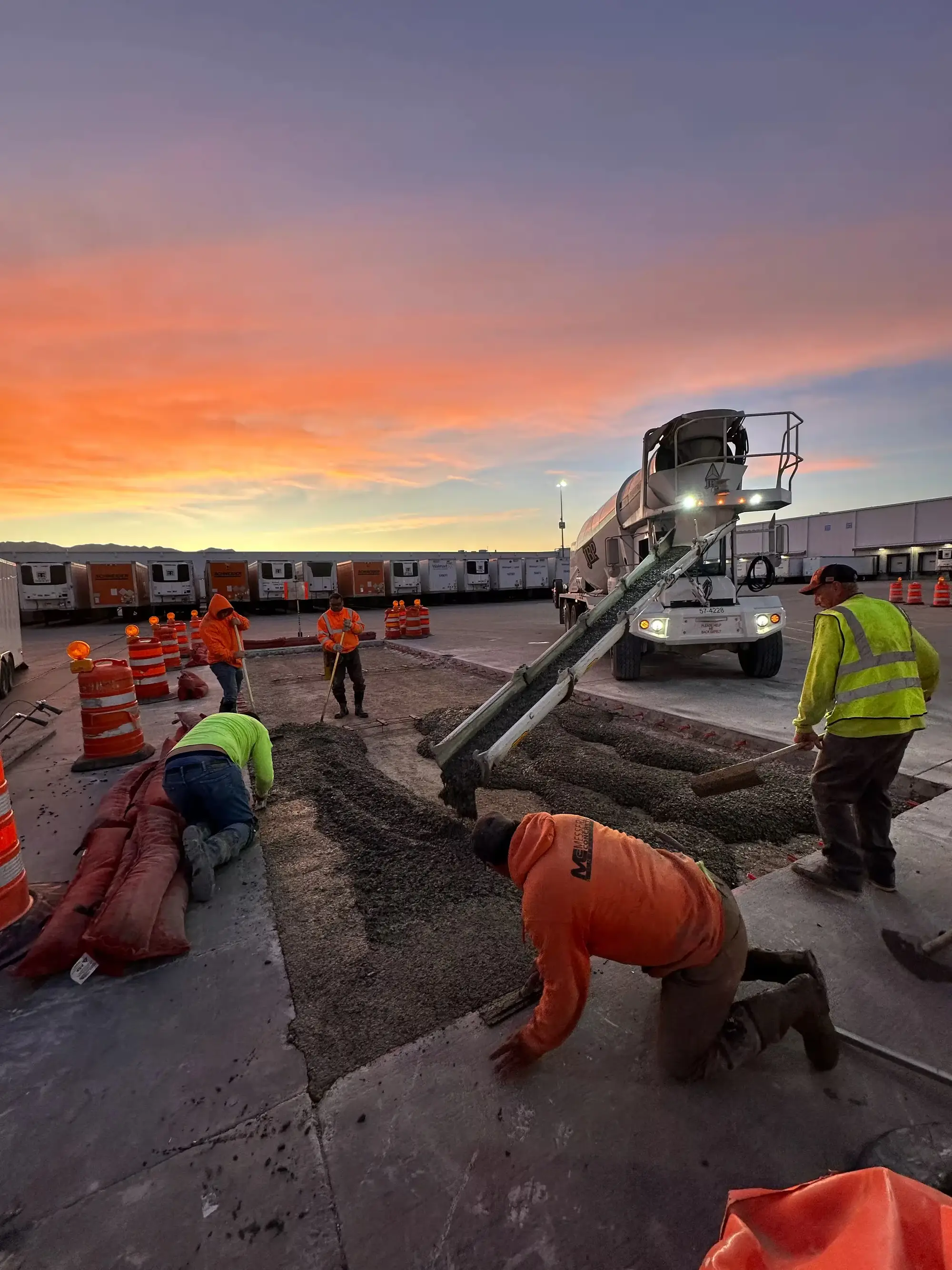 B Hansen Construction crew spreading concrete from a mixer truck under an orange sky